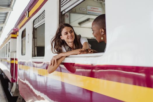 两名女子从火车车窗探出头，在车站里愉快地交谈