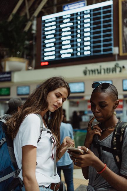 First-time travelers in Cat Ba checking itinerary, weather app, ferry schedule, and hotel booking, realistic candid travel problem-solving scene