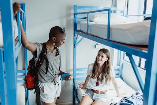 Two young women talking in a bright hostel room with bunk beds.