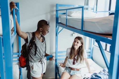 Free Two young women talking in a bright hostel room with bunk beds. Stock Photo