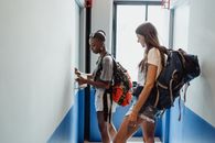 Woman in Blue Denim Shorts and Brown Backpack Standing Beside Woman in White Tank Top