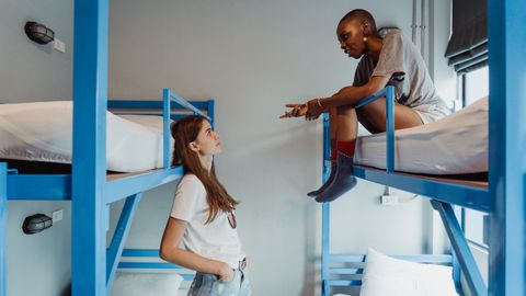 Two women engaging in conversation on bunk beds in a modern dormitory room.