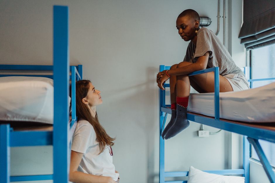 Two women having a friendly chat in a hostel bunk bed room, creating a relaxing atmosphere.