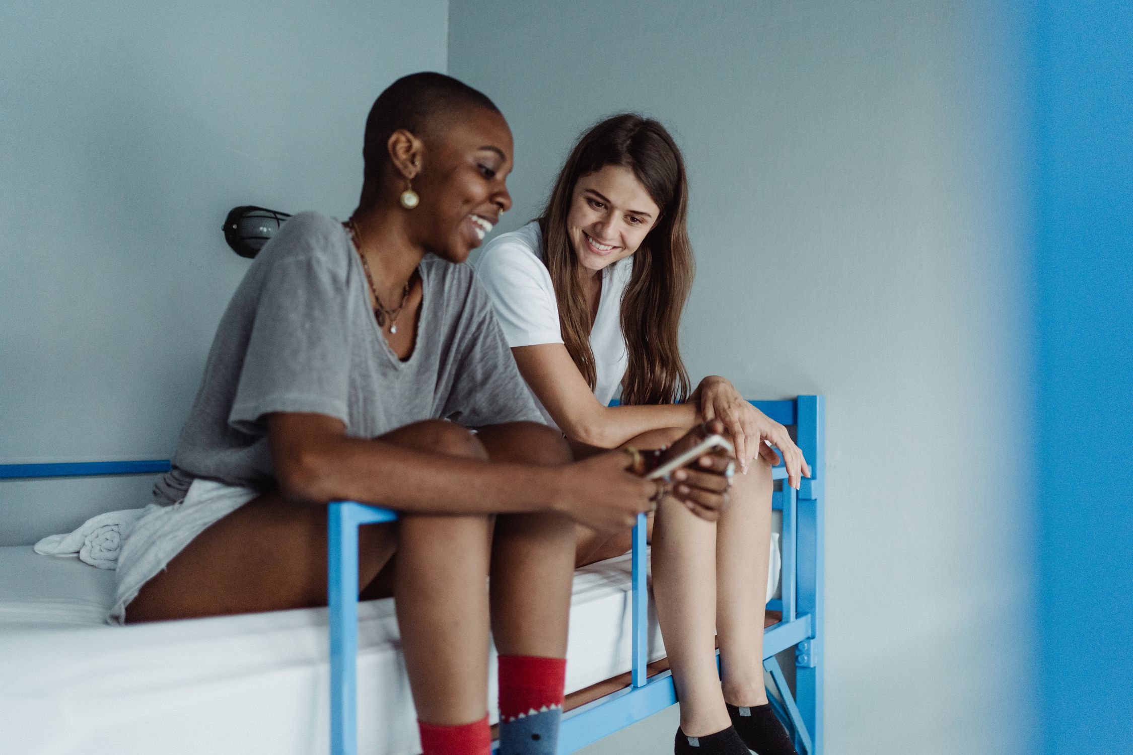 Two women relax and chat on a bunk bed in a modern hostel room, sharing a moment of connection.