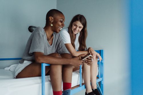 Free Two women relax and chat on a bunk bed in a modern hostel room, sharing a moment of connection. Stock Photo