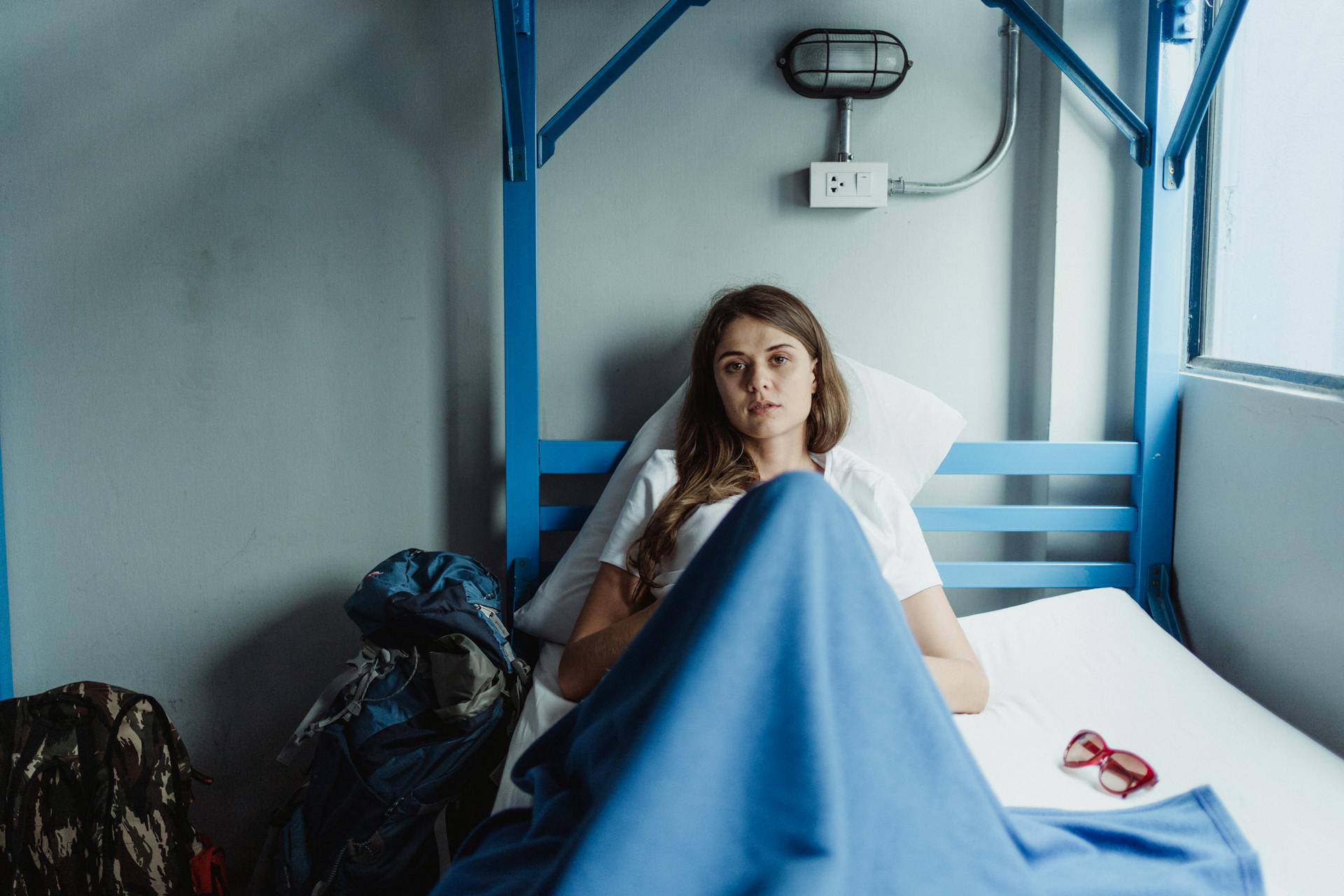 A young woman lying on a bunk bed with luggage in a cozy hostel room.