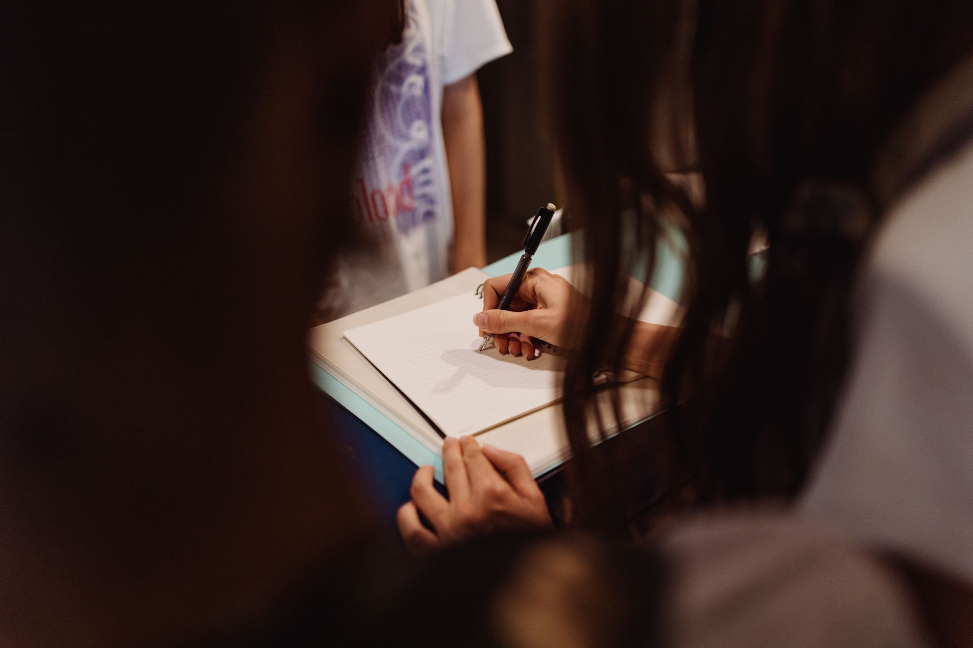 A woman writing in a notebook with a pen, focused and engaged.