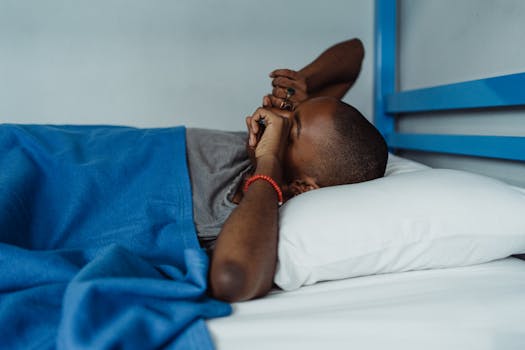 Black adult lying in bed, wrapped in a blue blanket, enjoying a lazy morning.