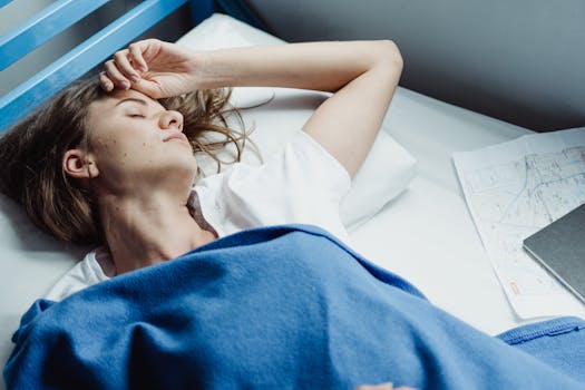Adult woman sleeping on bunk bed with blue blanket in a hostel.