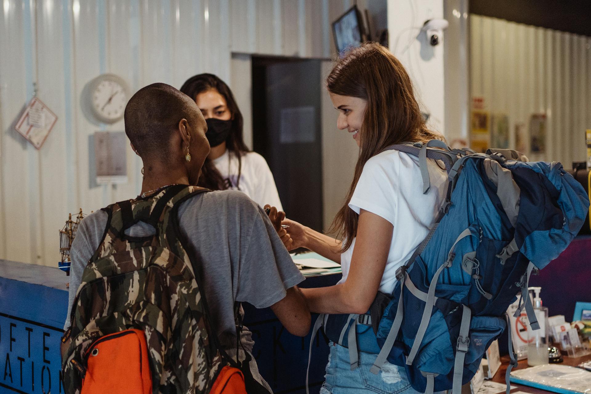 Diverse travelers with backpacks checking in at a lively hostel reception.