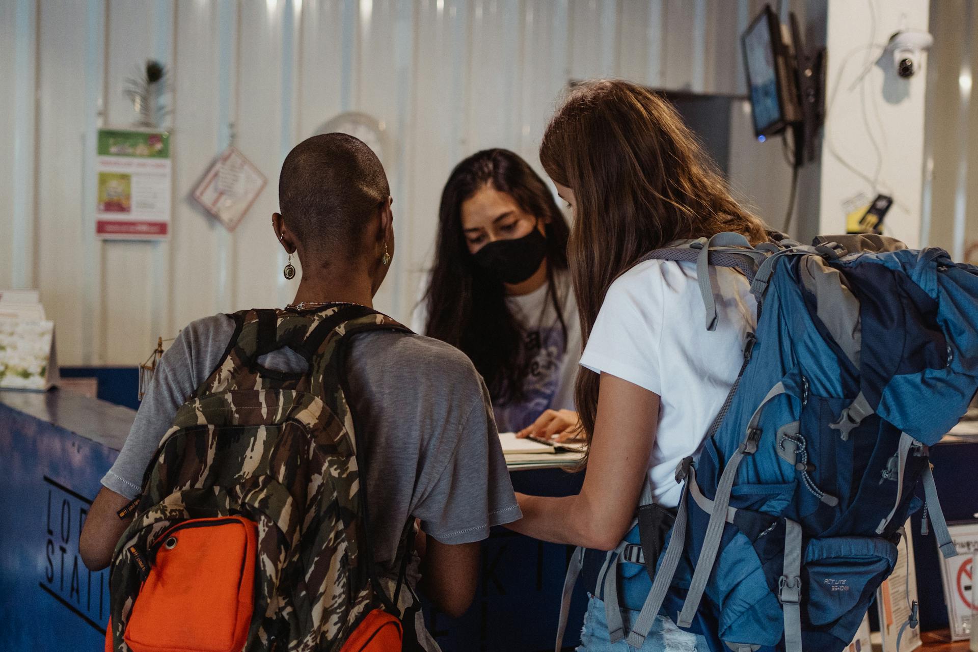 Two travelers with backpacks check in at a hostel reception counter.