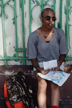 A tourist with a map sitting next to a backpack on a sunny day.