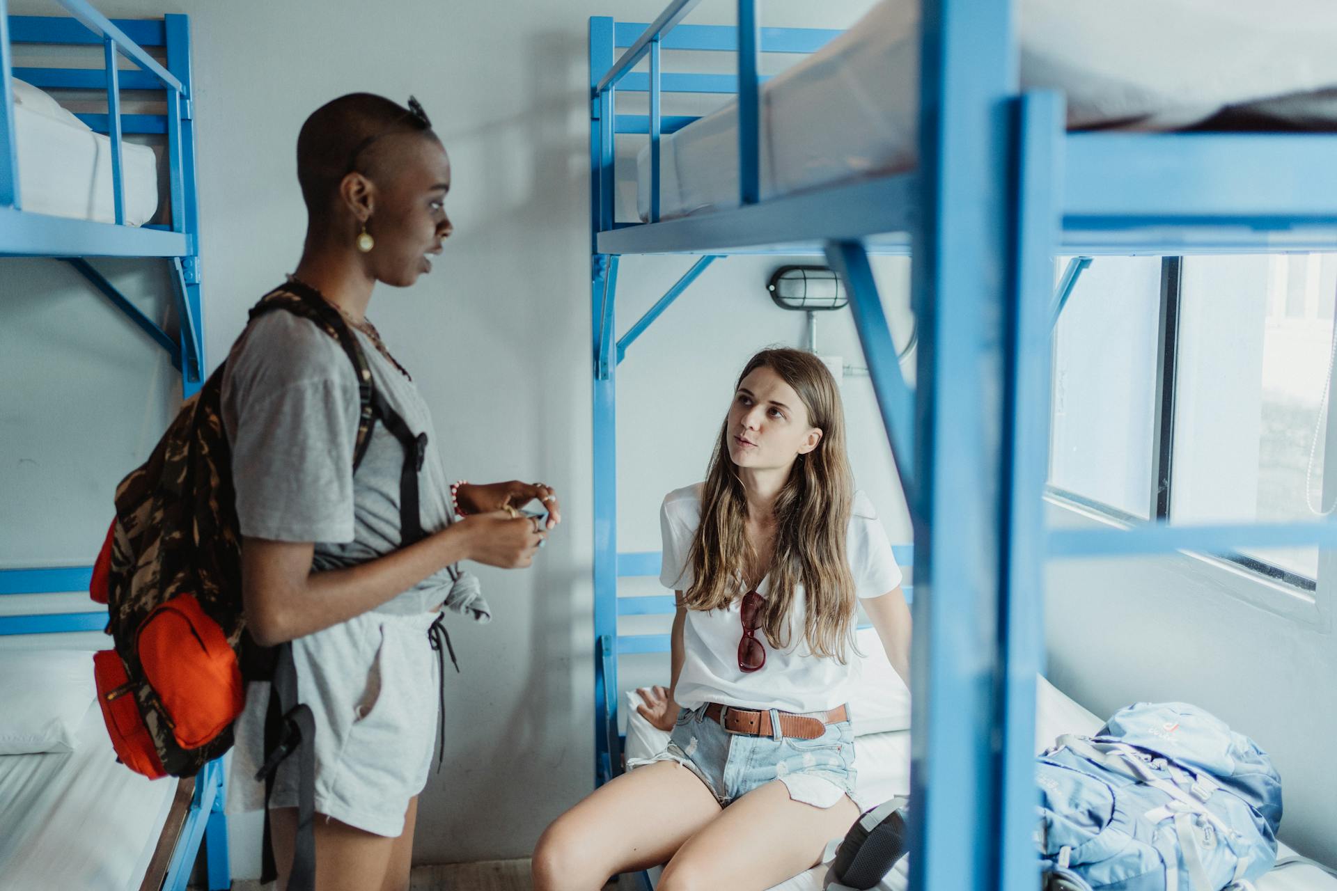 Two travelers converse in a hostel dormitory, showcasing diverse culture and adventure.