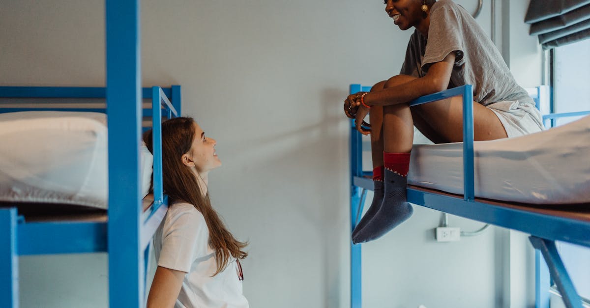 Two young women enjoying a casual conversation in a modern hostel room with bunk beds.