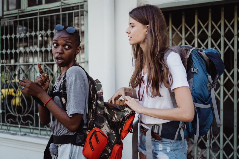 Two diverse women with backpacks engaged in conversation, exploring an urban setting.