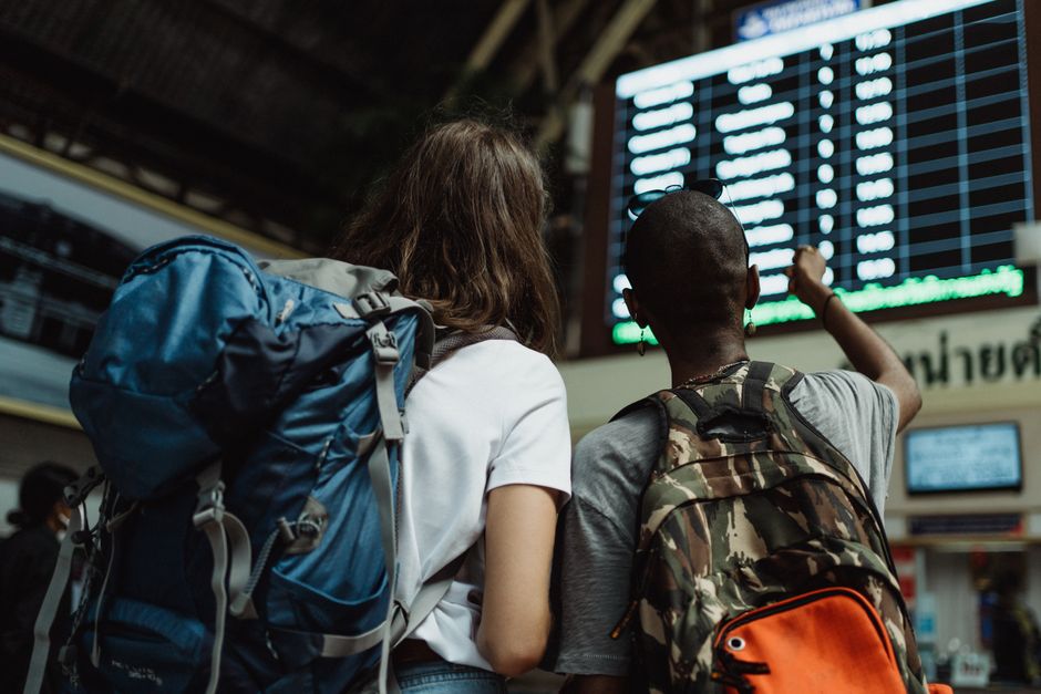 Como Transformar Suas Viagens em Experiências Inesquecíveis 2 Two backpackers checking the digital board at a train station for travel information.
