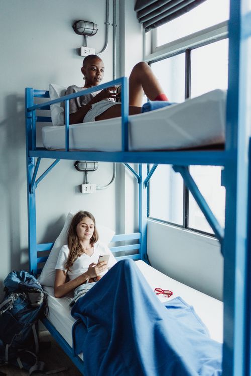 Free Two women relaxing on bunk beds inside a room, using smartphones. Stock Photo