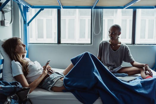 Two young women having a conversation in a hostel room with natural light streaming through windows.