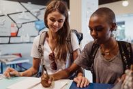 Two Women with Backpacks Writing in a Guest Book in Hostel