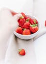 From above of crop person taking fresh strawberry from bowl on fabric on table