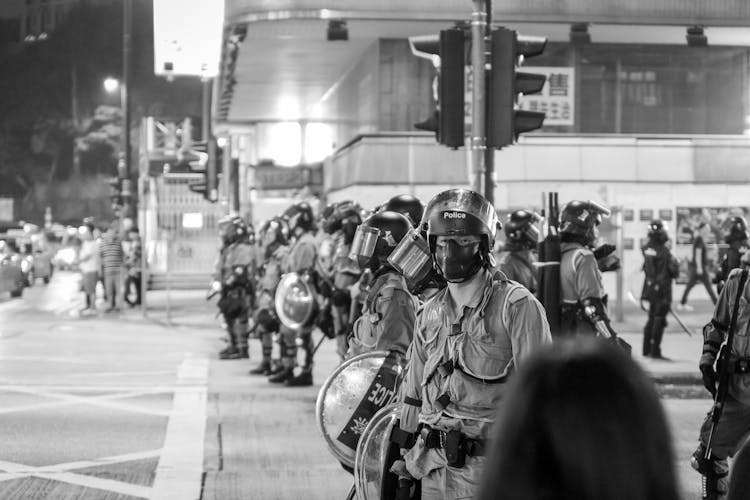 Police In Uniforms, Helmets And Holding Shields On A Street 