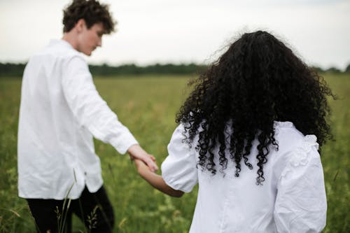 Man and Woman Holding Hands While Walking on Green Grass Field