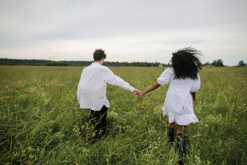 Free Man and Woman Holding Hands While Walking on Green Grass Field Stock Photo