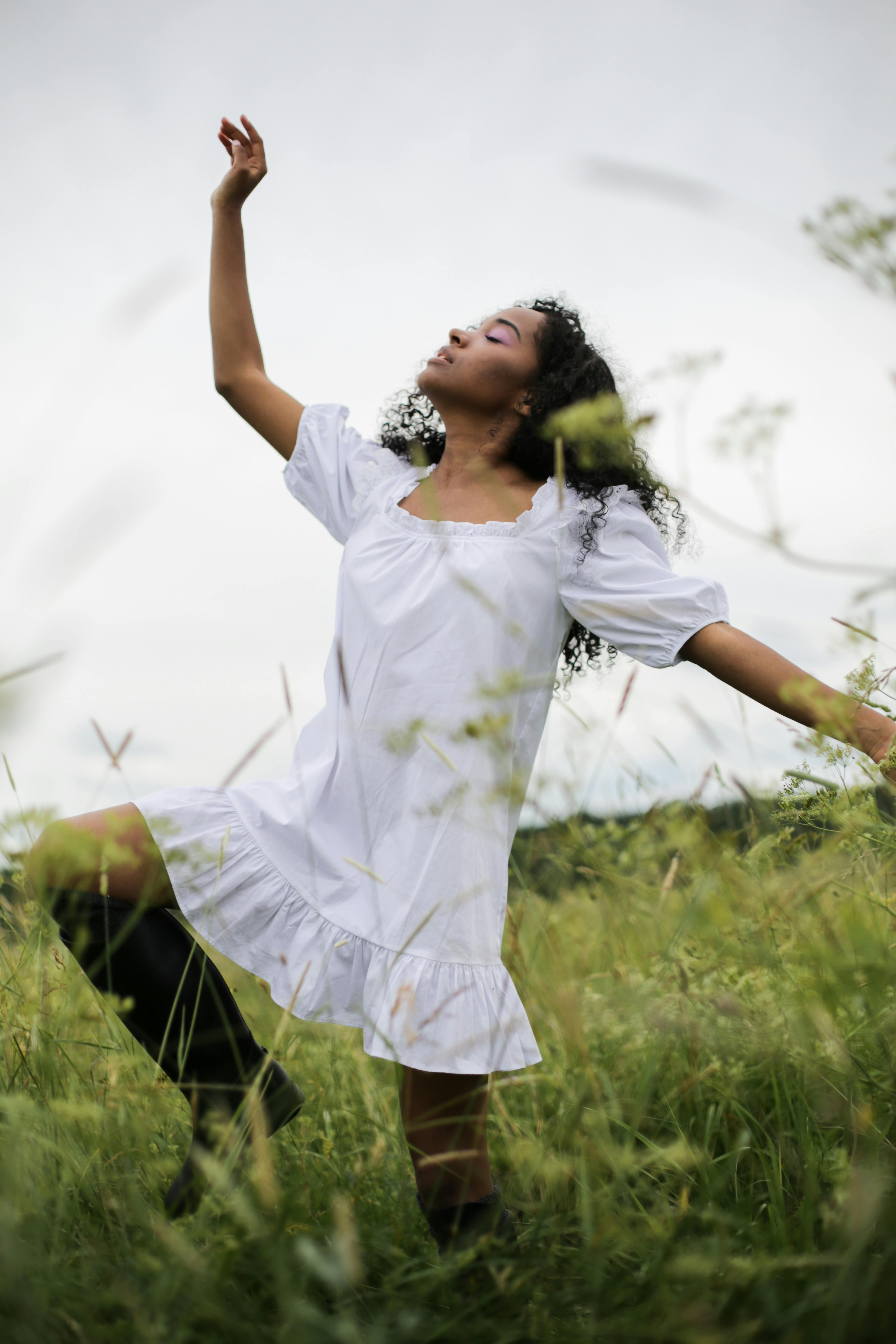 夏日郁郁葱葱的草地上，一位身着白色连衣裙的女子正优雅地起舞