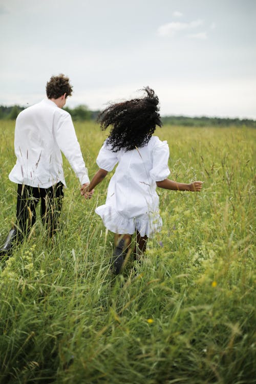 Free Man and Woman Holding Hands While Walking on Green Grass Field Stock Photo