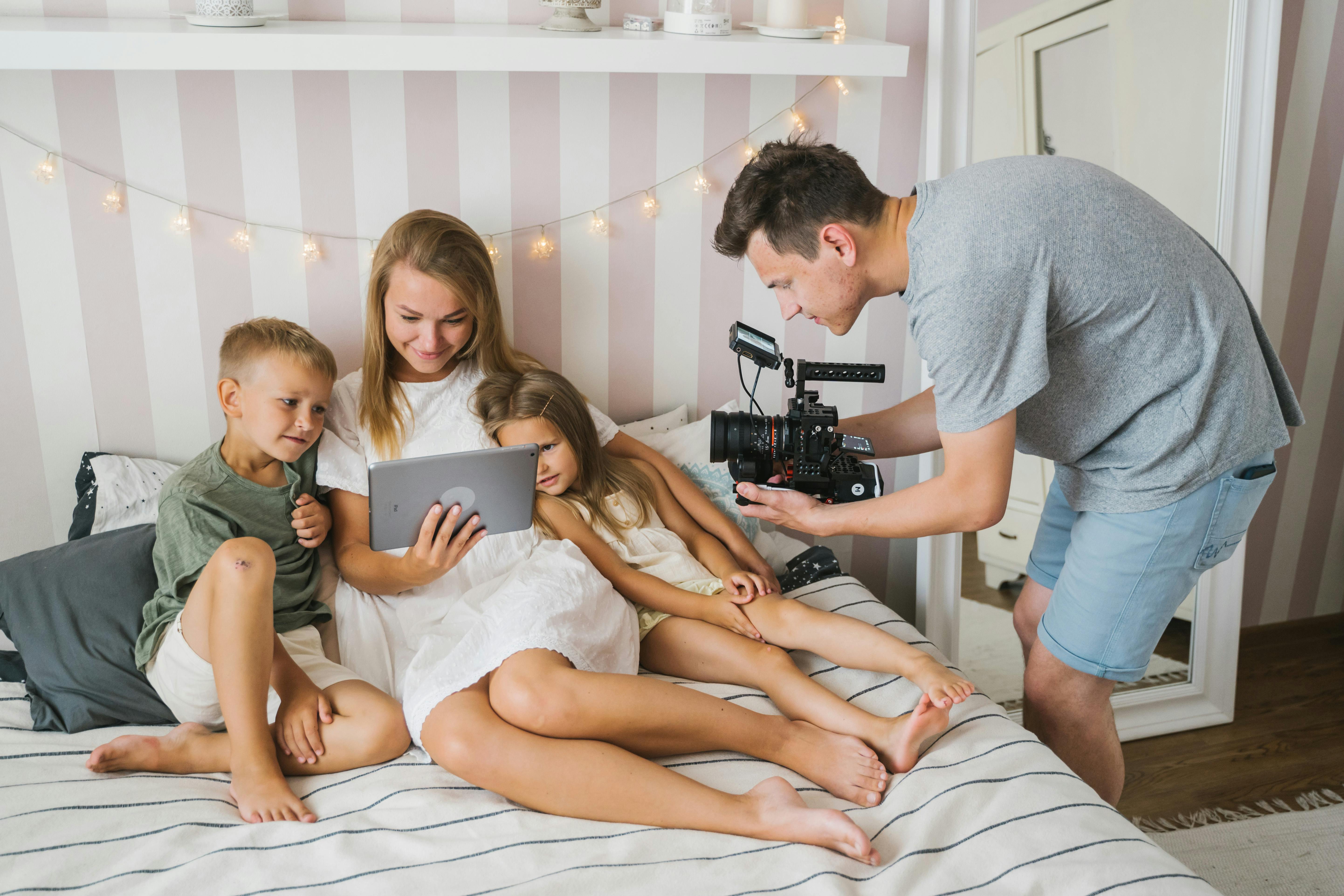 Family enjoying quality time with tablet and camera in a cozy bedroom setting.