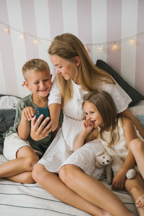 Free A mother and her two children are happily sitting together indoors, sharing a moment with a smartphone. Stock Photo