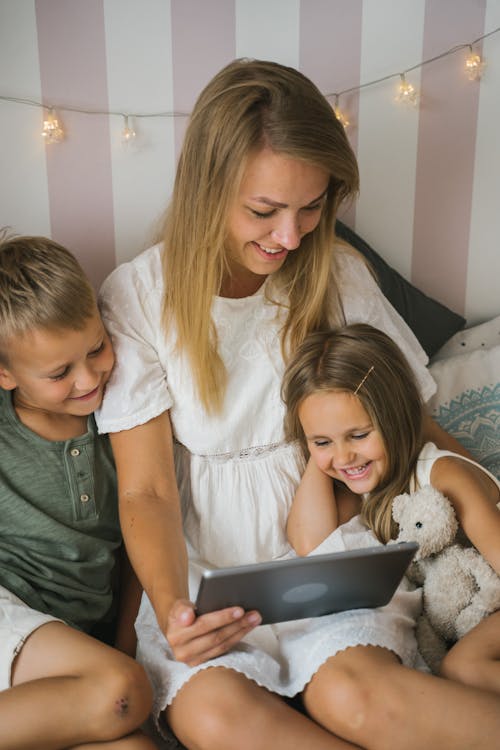 A Woman in White Dress and Two Kids Looking at the Screen of a Tablet