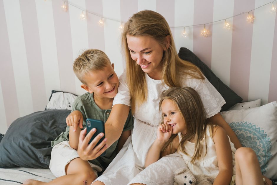 Madre e hijos disfrutando de un momento feliz, compartiendo sonrisas mientras miran un teléfono inteligente en el interior.