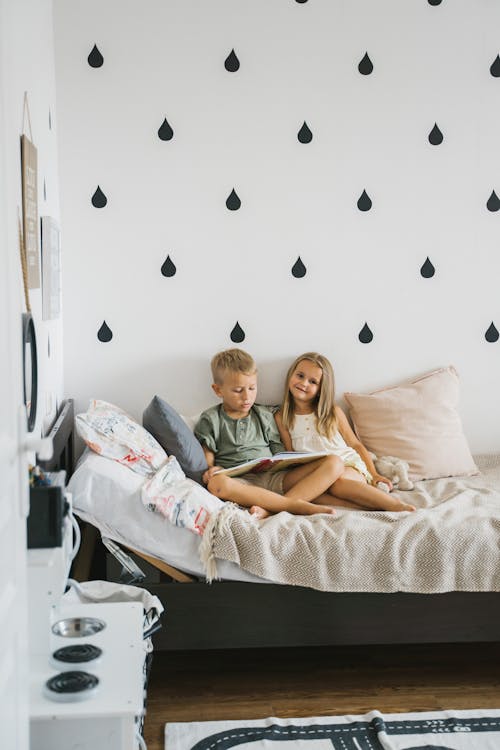 Free Photo of Siblings Reading a Book on the Bed Stock Photo