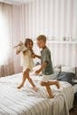 两个兄弟姐妹在舒适的房间里，愉快地跳上床嬉戏，笑声不断