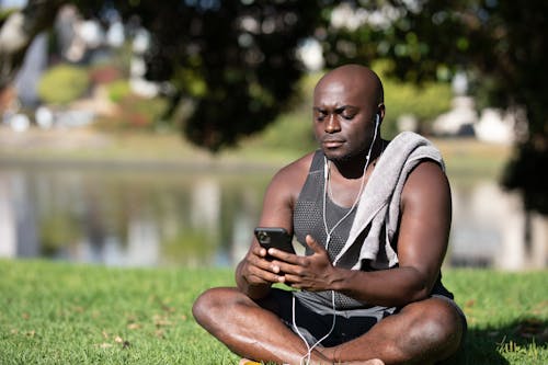 Free A Man Sitting on Grass Using His Black Smartphone Stock Photo
