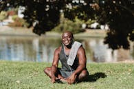 在阳光明媚的公园湖边，一个戴着耳机、拿着毛巾的人正放松地微笑着