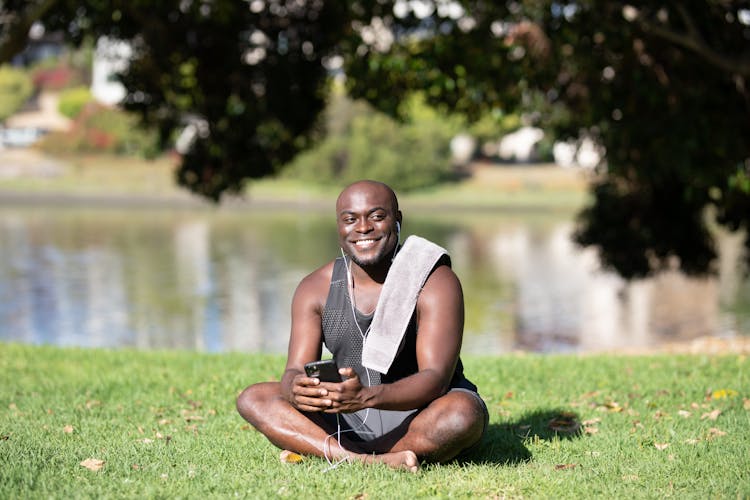 A Man Sitting On Green Grass Holding His Phone