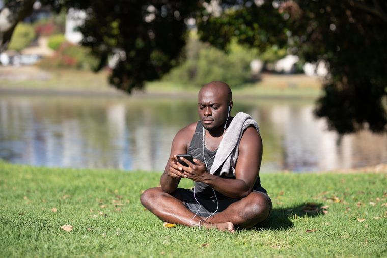 Man sitting on grass by a lake checking his phone — photo by Ketut Subiyanto on Pexels