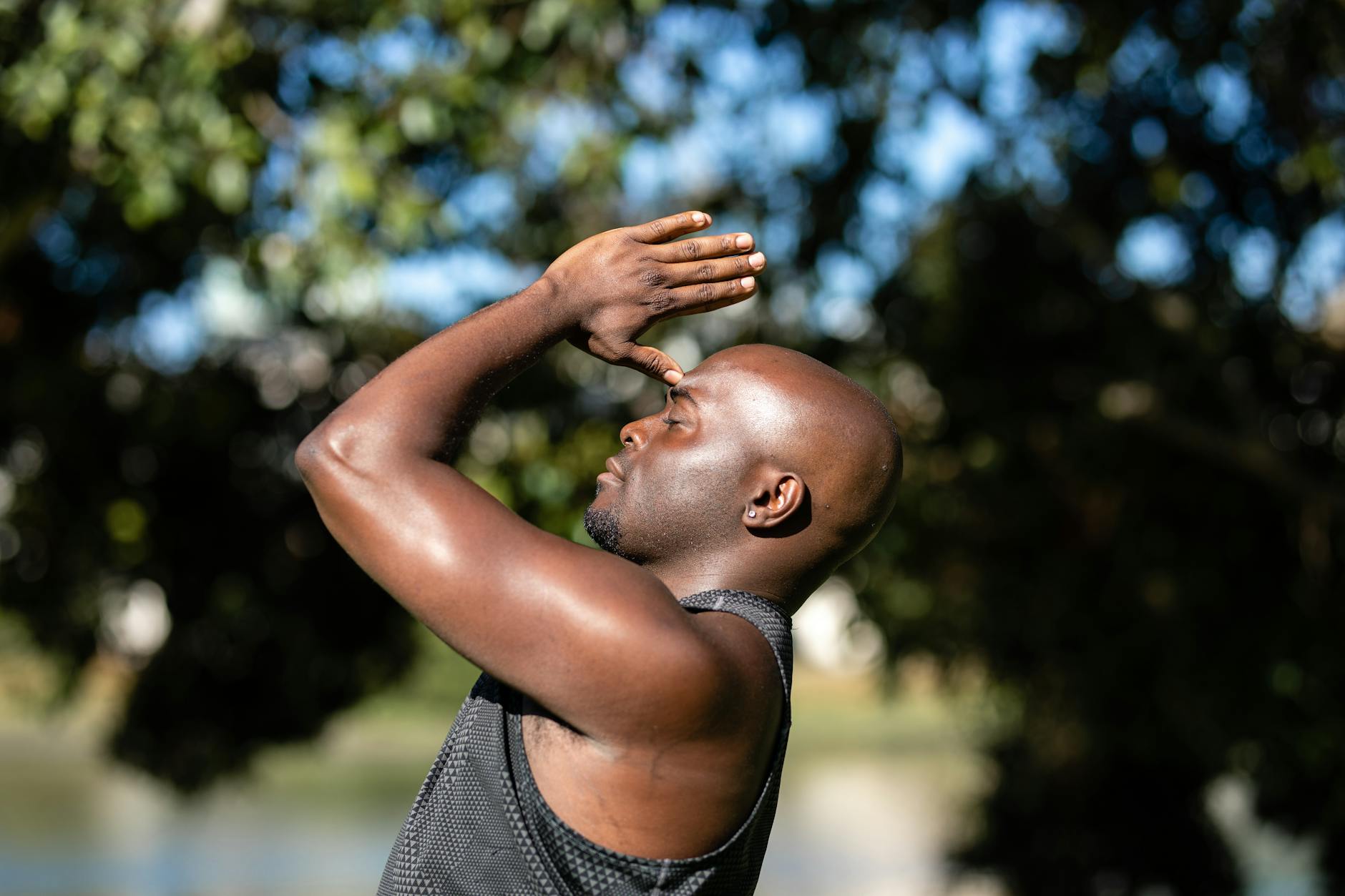 A bald man meditating and practicing yoga outdoors with a blurred natural background.