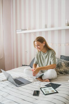 Woman enjoying an online education session while seated comfortably on her bed, using a laptop.