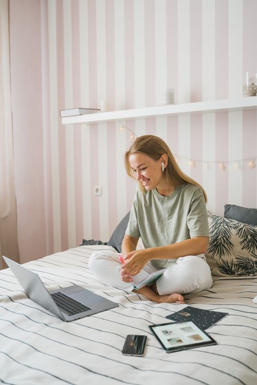 Free Woman enjoying an online education session while seated comfortably on her bed, using a laptop. Stock Photo