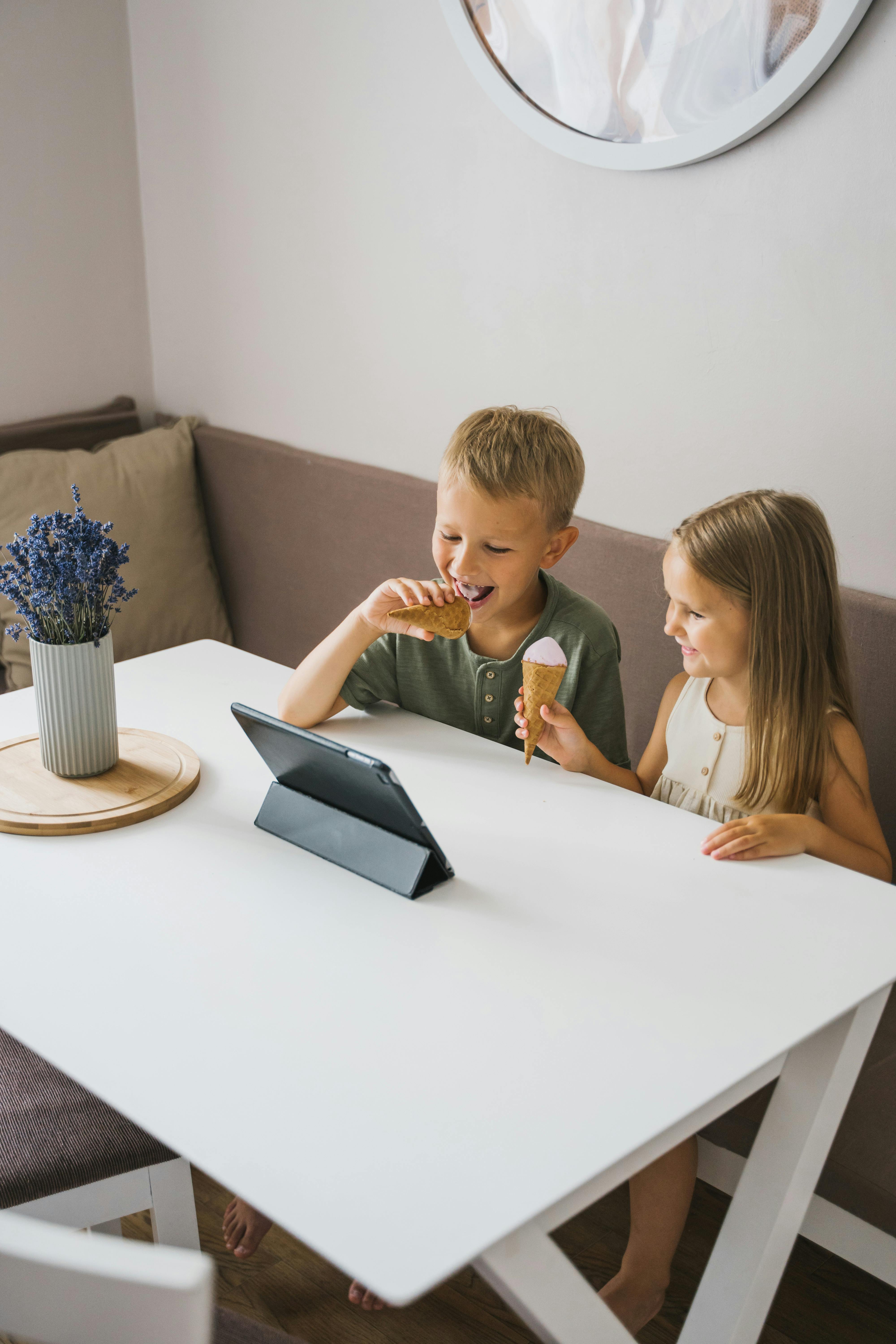 children holding ice cream cones while looking at the screen of a tablet