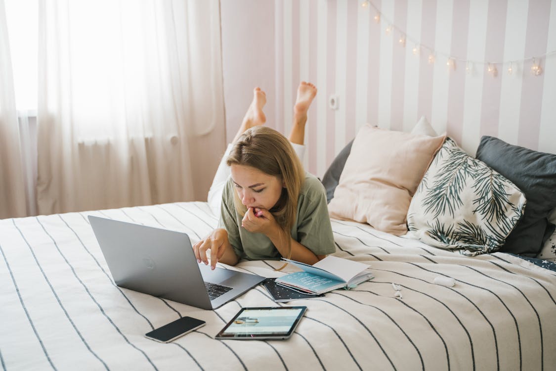 Woman in Green Shirt Using Macbook Air on Bed in remote work