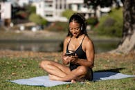 一名穿着运动服的妇女在阳光明媚的公园里，坐在瑜伽垫上使用智能手机