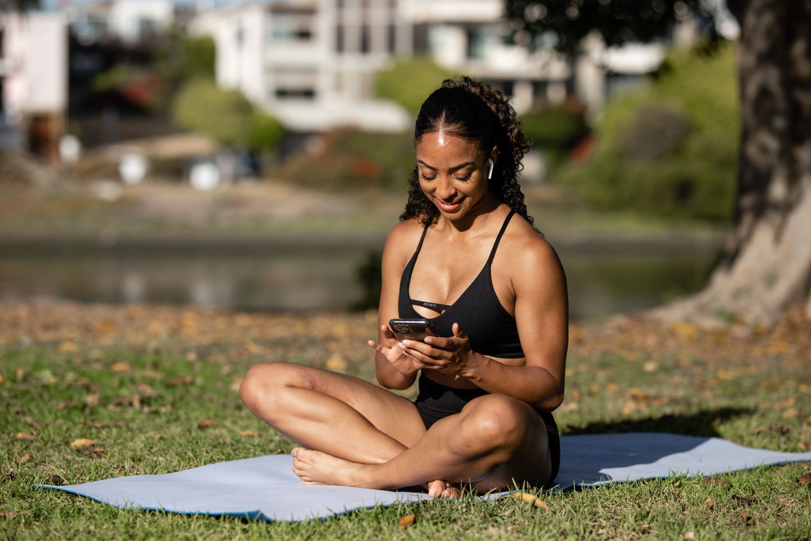 Woman sitting on a yoga mat outdoors checking a yoga app on her smartphone