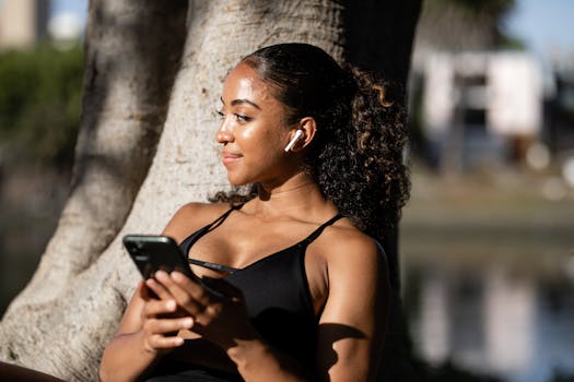 Young woman in sportswear relaxing outdoors, using smartphone and wireless earbuds.
