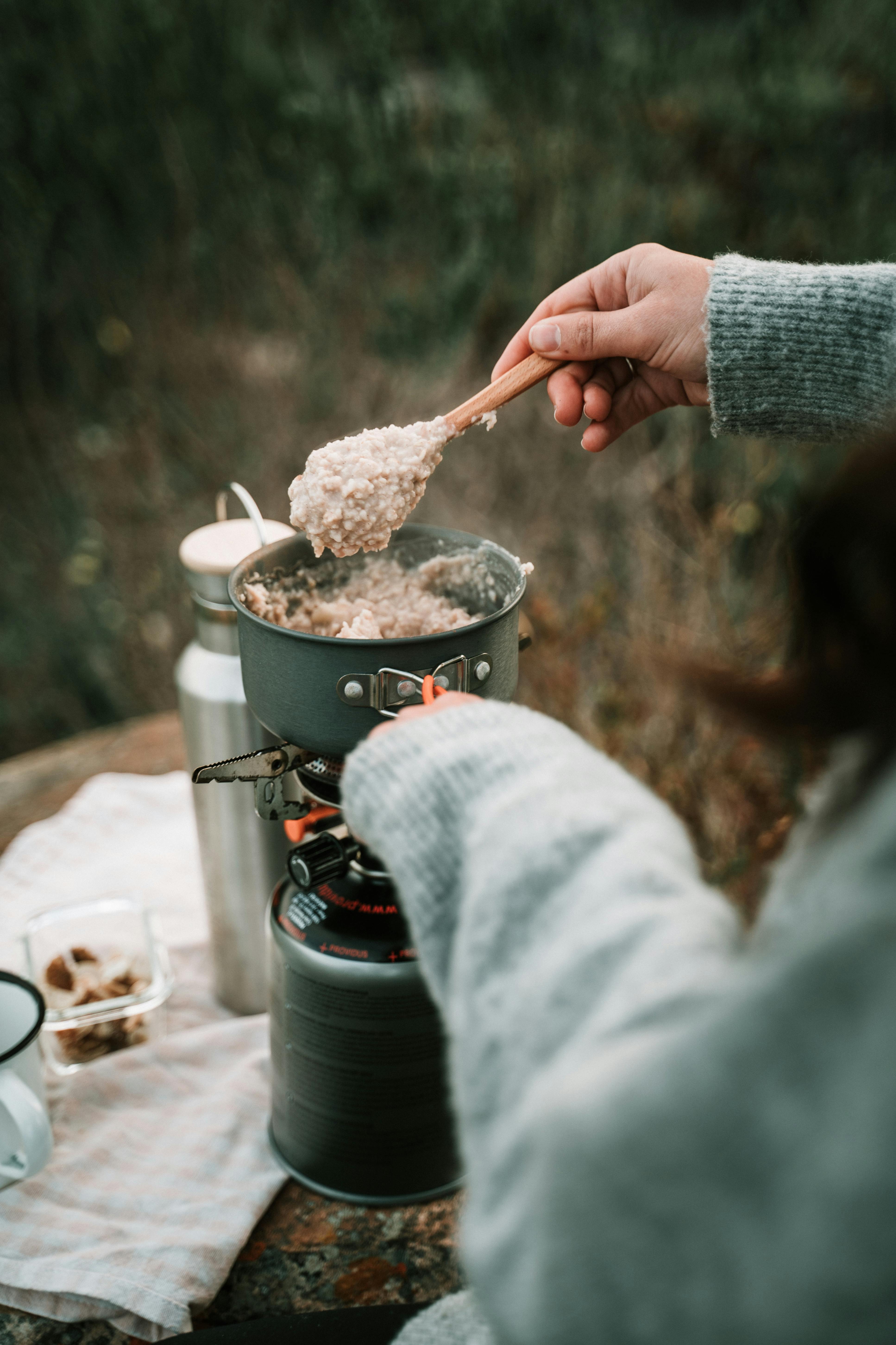Person cooking oatmeal outdoors with camping stove and pot.