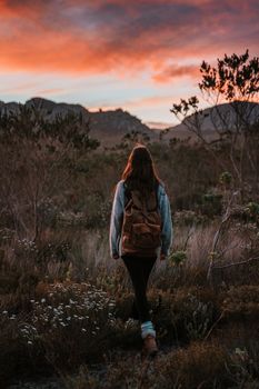 日落时分，一位背着背包的女子徒步穿越风景如画的山脉，天空充满活力