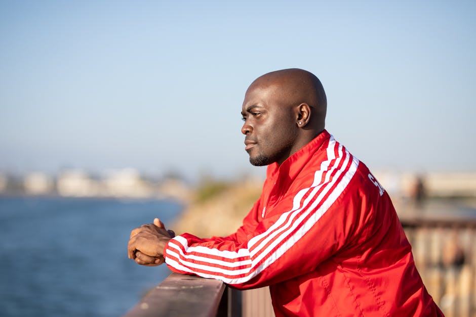 African American man in red jacket looking out over a waterfront with a pensive expression.